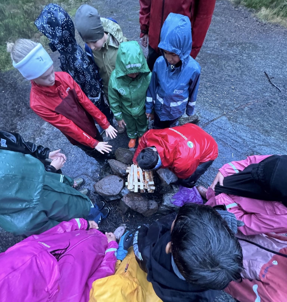 En gruppe elever i regntøy som tenner bål